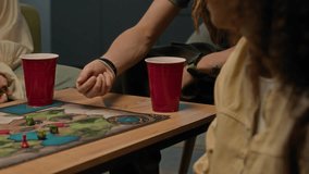 Tilt up slowmo shot of cheerful Caucasian guy with long dreadlocks raising plastic red cup in toast in middle of tabletop gaming process with group of diverse friends in apartment - Powered by Shutterstock - Get 15% off with code: PIKWIZARD15