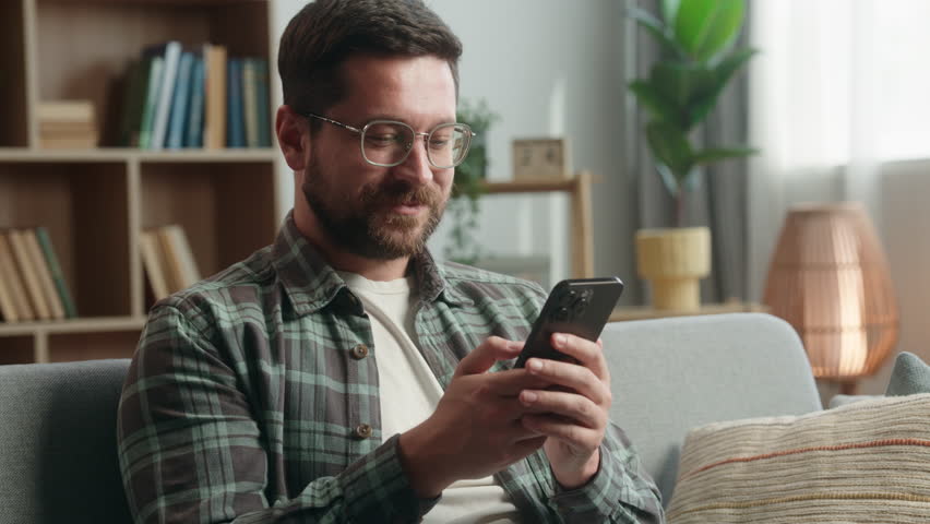 At home smiling gadget addict man guy male using mobile phone app smartphone social media receive message offer good news showing thumb up recommend internet service order food delivery like gesture