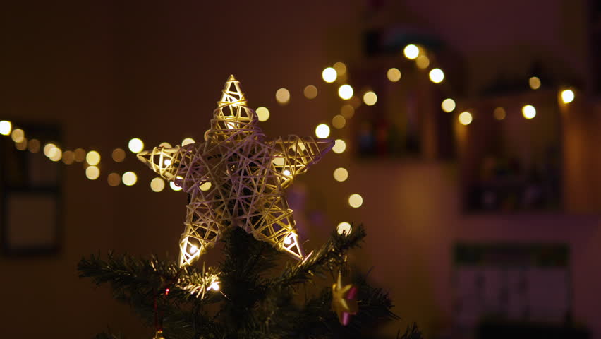 Background eco top of star on Christmas tree in decorated room at night. Five-pointed star made of natural rattan in light of garlands in interior of apartment on Christmas Eve.