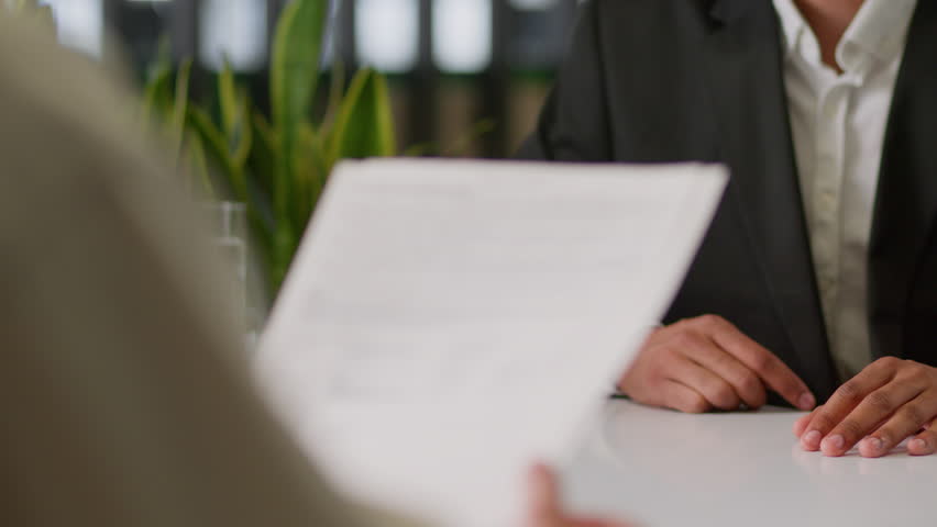 Two unrecognizable business colleagues businessmen men male guys multiracial in office signing paper sign contract document bank insurance table banking credit investment company agreement signed pen