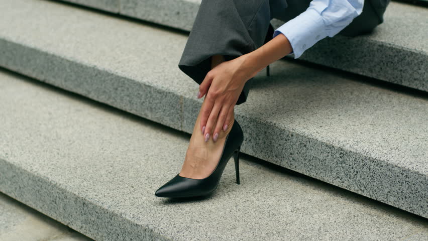 Tired exhausted African American woman female lady girl business employer businesswoman in city sitting office stairs stairway suffer ankle ache foot pain stress upset discomfort high heels shoes
