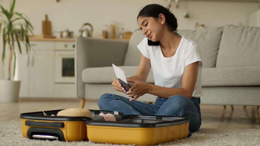 Hindu woman Indian girl Arabian female at home prepare for trip vacation travel talking call talk smartphone mobile phone packing clothes in suitcase baggage holding tickets airline airport passport