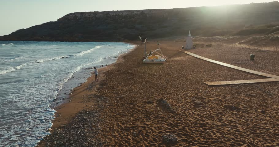 Aerial view of Ramla beach on the island of Gozo, Malta. A woman walks on the beach on the shore of the Mediterranean Sea at sunset. Travel and tourism. High quality 4k footage