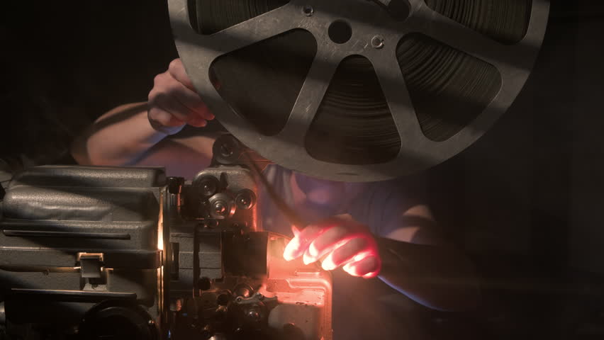 Man Installs reel of film into vintage movie projector.