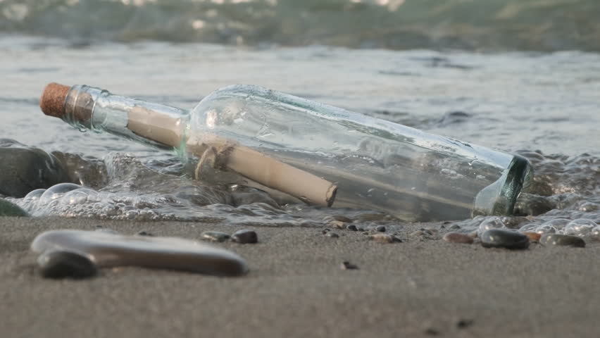 Glass bottle with paper note message inside on beach of sea.