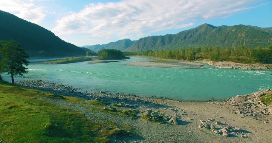 4K aerial point of view. Low altitude flight over fresh fast mountain river with rocks at sunny summer morning. Green pine trees and sun rays. Pure cold water stream.