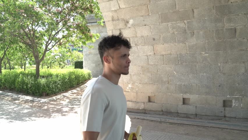 Young hispanic man with relaxed expression eating banana at street