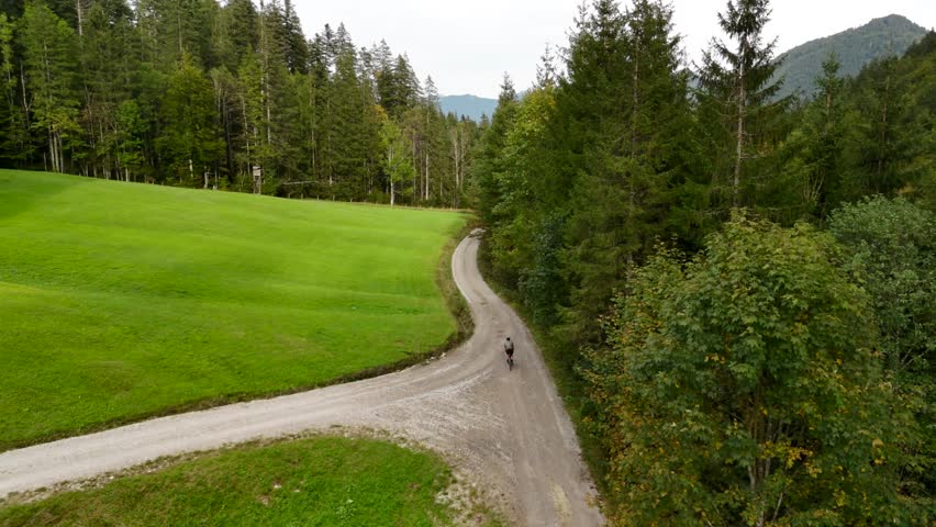 Aerial view of male cyclist riding gravel bike in September in Bavaria, Germany in forest. Drone view of bicyclist from behind riding along gravel bike route in Bavarian forest in the mountains. 