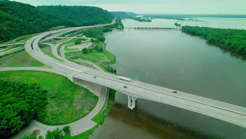 Aerial shot dry van truck driver on Dresbach Bridge over the Mississippi River, surrounded by lush greenery and waterways.