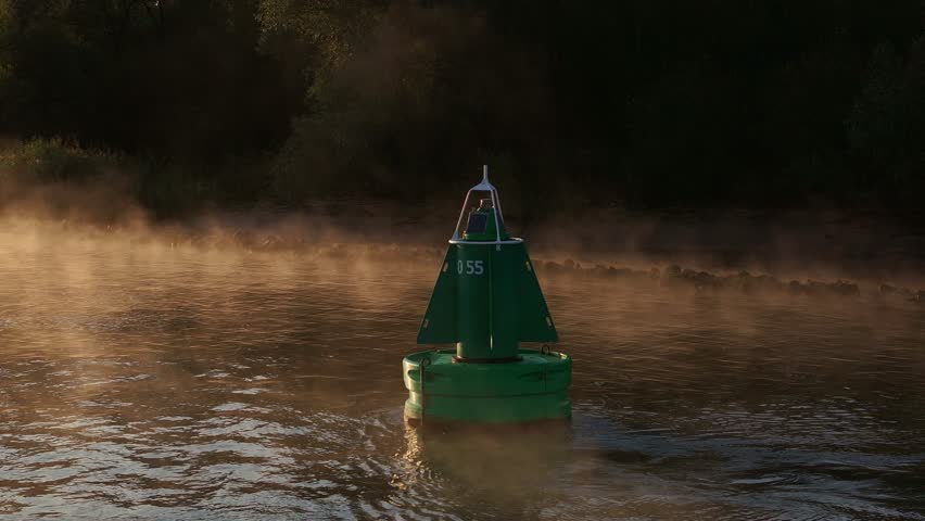 Misty morning fog rises over the river, creating a mysterious and serene atmosphere around green buoy at sunrise