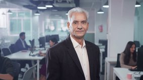 A movement shot of a confident senior male entrepreneur or businessman in formal attire standing with crossed arms, looking at the camera, smiling in a corporate office start up business workplace - Powered by Shutterstock - Get 15% off with code: PIKWIZARD15