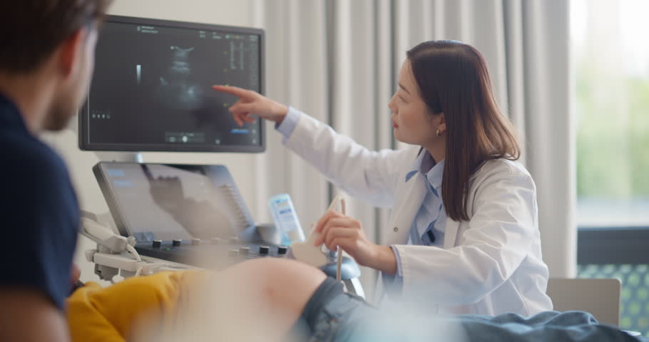 Asian Obstetrician Performs Ultrasound on Pregnant Patient, Explaining Baby Development. Modern Medical Equipment Displays Detailed Sonogram Images as Doctor Gestures Towards Screen