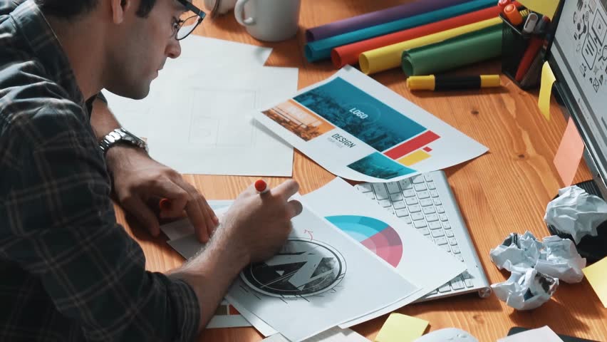 Professional designer writing and designing logo graphic at meeting. Closeup of business man working on colored palettes and writing idea on sticky notes on table with equipment and paper. Symposium.