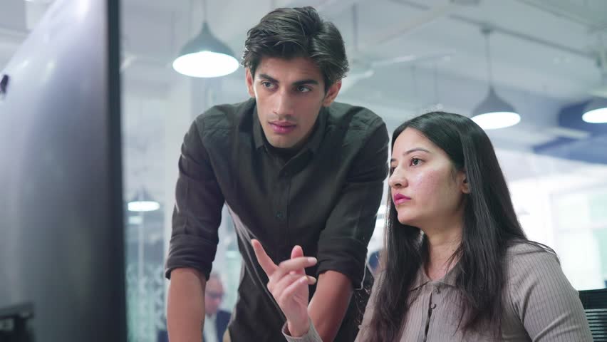 Young attractive male and female corporate office colleagues or coworkers discussing, brainstorming, and busy working together on an assignment using a computer in a modern start up business workplace