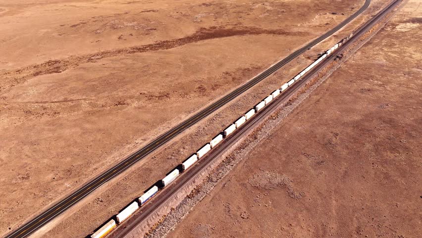 Aerial ascending view of american freight train with double stacked containers pulled by three diesel locomotive engines, high desert of Arizona, alongside the route 66 between Flagstaff and Seligman.
