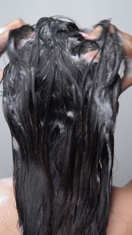 Back view of a young Asian woman with long hair, getting her hair washed using shampoo, isolated by white background.