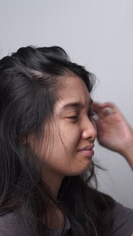 Close up footage of a young Asian woman pointing to the dandruff on her hair.