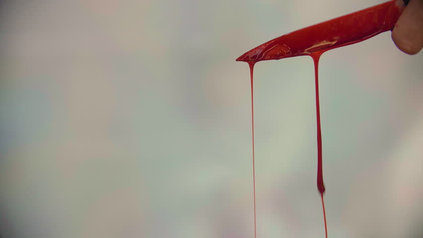 A mysterious murderer holds blood-covered knife, dripping with red, the background in unclear and blurry..