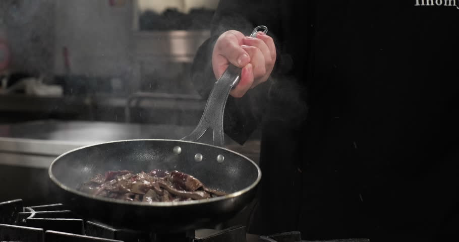 Close-up chef preparing beef liver in a frying pan on a gas stove, throwing in the air. Slow motion
