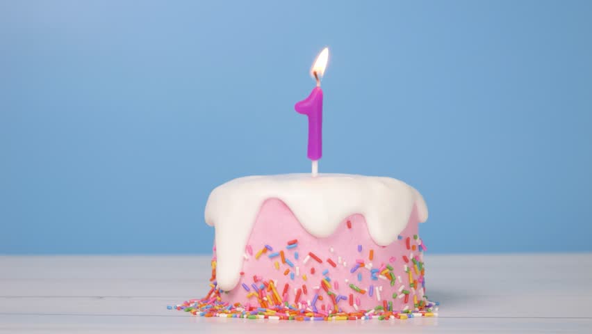 birthday cake with number one candle to celebrate 1st birthday, seamless looping of cute cake with colorful candle number 1 for birthday annual celebrate party was lit, blue background