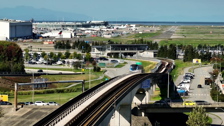 A SkyTrain Glides along an Elevated Track, with Planes and Runways in the Background Close to YVR in British Columbia, Canada - Static Shot