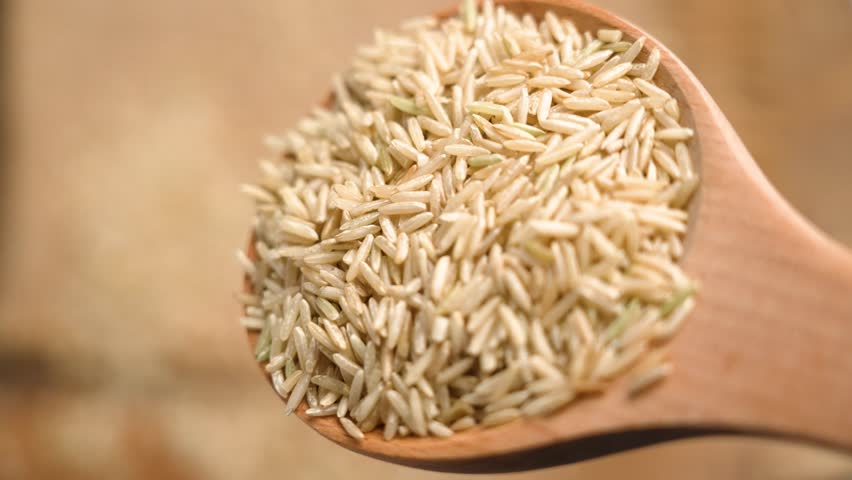 Close up of coarse basmati integral rice spilling from a rustic biodegradable wooden spoon. Burlap fabric softly blurs in the background. Slow motion