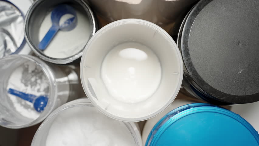 Overhead view of Protein Powder being scooped into a container with milk, multiple jars of different supplements for customized nutrition. Slow motion.