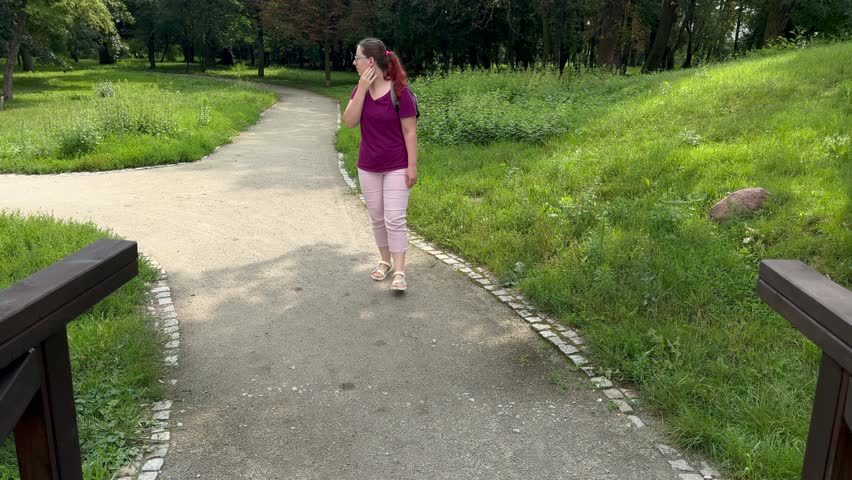 Woman walking across wooden bridge in park with backpack, surrounded by nature on sunny day. Time for self-reflection and relaxation. Concept of healthy lifestyle, physical activity 