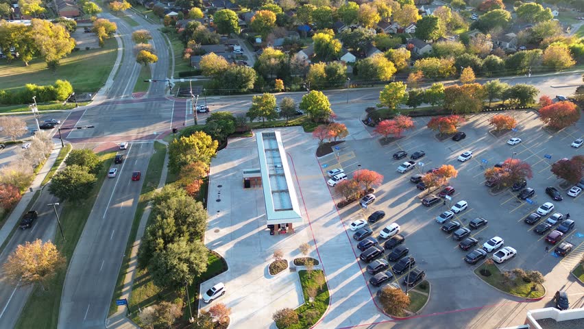 Busy road intersection in residential neighborhood with corner gas station of grocery store, colorful fall foliage autumn leaves in Coppell, suburbs Dallas, cluster single-family house, flyover. Texas