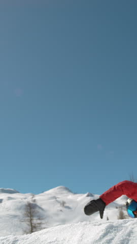 SLOW MOTION, LENS FLARE, CLOSE UP: Young pro snowboarder jumps off kicker and does a spinning trick. Spectacular shot of winter athlete riding his snowboard and doing a grab high in the sunny sky.