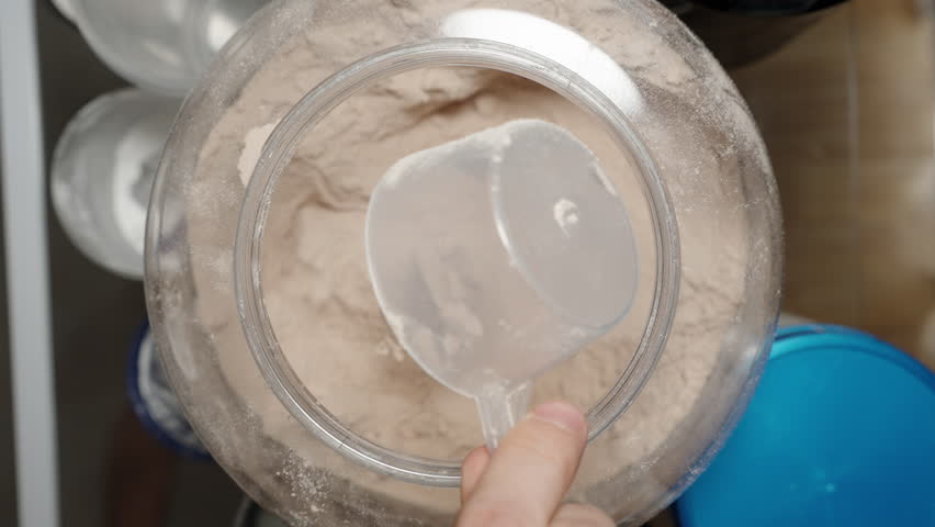 Athlete scooping Protein Powder from a large container, preparing to add it to a shaker for a post-workout shake. Slow motion.