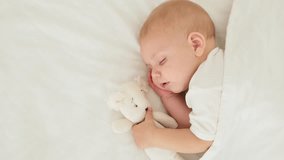 a newborn baby sleeps sweetly holding a toy in his hands, a place for text, a baby sleeps on a white bed under a blanket with a pen under his cheek, a healthy baby's sleep - Powered by Shutterstock - Get 15% off with code: PIKWIZARD15