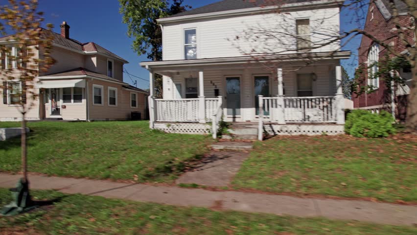 Moving passenger car window perspective of American landscape full of rural suburban neighborhood by Americana town, including homes, townhouses, apartments, small businesses, and lawns in fall autumn