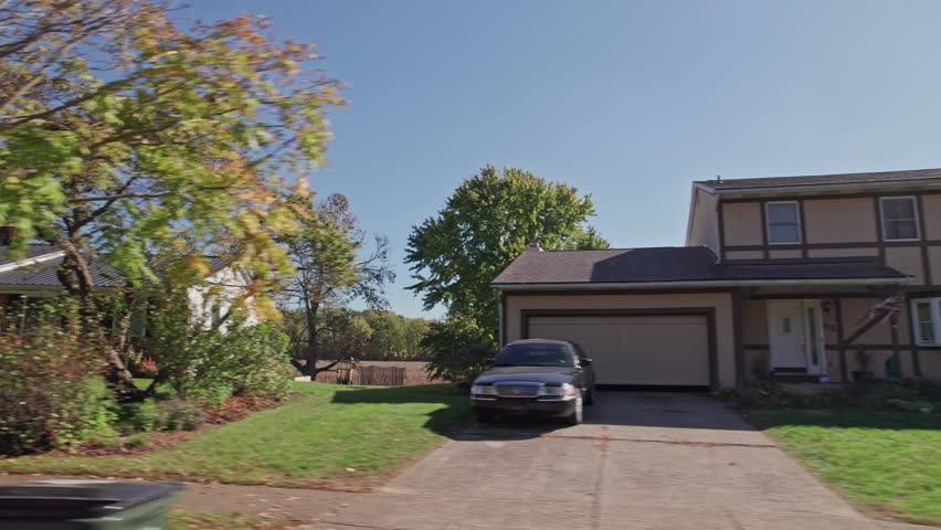 Moving passenger car window perspective of American landscape full of rural suburban neighborhood by Americana town, including homes, townhouses, apartments, small businesses, and lawns in fall autumn