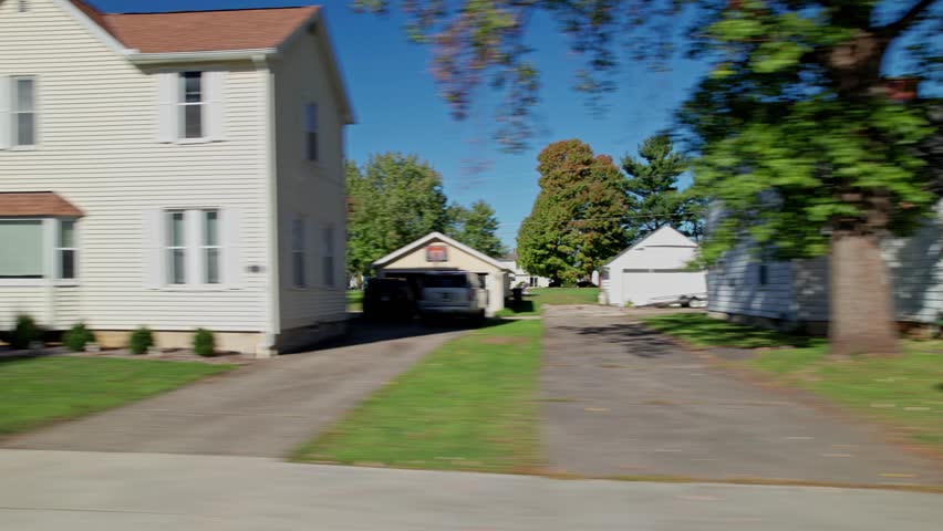 Moving passenger car window perspective of American landscape full of rural suburban neighborhood by Americana town, including homes, townhouses, apartments, small businesses, and lawns in fall autumn