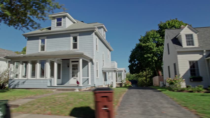 Moving passenger car window perspective of American landscape full of rural suburban neighborhood by Americana town, including homes, townhouses, apartments, small businesses, and lawns in fall autumn