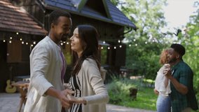 Multiracial couple is embracing and smiling during a garden party, with string lights illuminating the background and friends dancing nearby, creating a warm and festive atmosphere - Powered by Shutterstock - Get 15% off with code: PIKWIZARD15