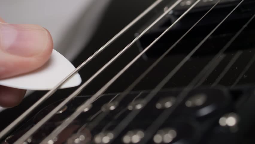 a pick plays the strings of an electric guitar in slow motion. Playing the guitar close-up