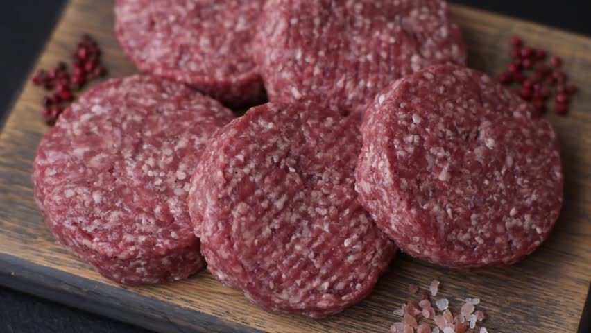 Fresh raw ground beef burger patty with salt and spices on textured concrete background