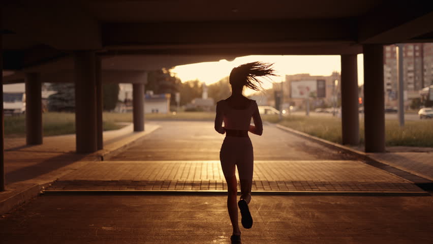 A young sporty woman runner is listening to music in earphones and training workout. Slim fitness girl is jogging outdoor. Concept of workouts running and healthy sport lifestyle