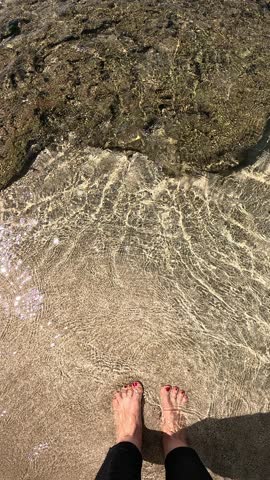 Female feet in transparent water on the beach. Red enamel
