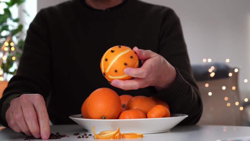 Pomander oranges with cloves made by woman at table with bokeh in background.