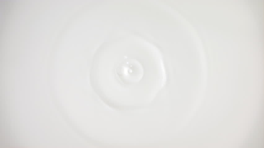 Fresh milk drop falling and splashing in a milky pool from above. Slow motion rings and ripple top view