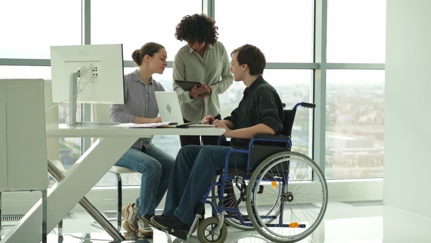 Teamwork brainstorm. Diverse multiracial colleagues man in chair for people with disability working together. Group of people sitting in creative office discussing business. Young professional team