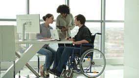 Teamwork brainstorm. Diverse multiracial colleagues man in chair for people with disability working together. Group of people sitting in creative office discussing business. Young professional team - Powered by Shutterstock - Get 15% off with code: PIKWIZARD15