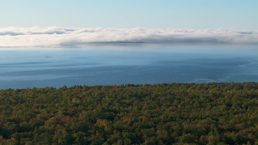 Morning drone view of fog banks covering Madeline island on Lake Superior with early fall south shore forest
