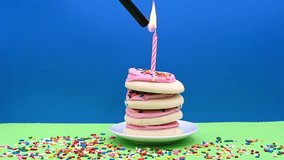 4K HD video of frosted sugar cookies stacked to form a cake, sitting on small round porcelain plate on green place mat with candy sprinkles. Hand reaches in lighting pink candle. Blue background. - Powered by Shutterstock - Get 15% off with code: PIKWIZARD15