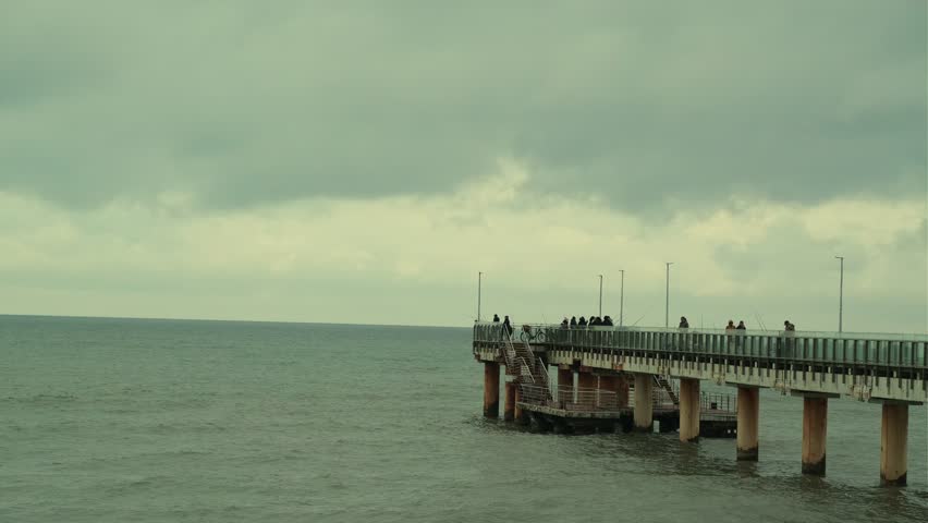 People Walking on a Pier Overlooking the Ocean at Dusk With Dramatic Clouds Above