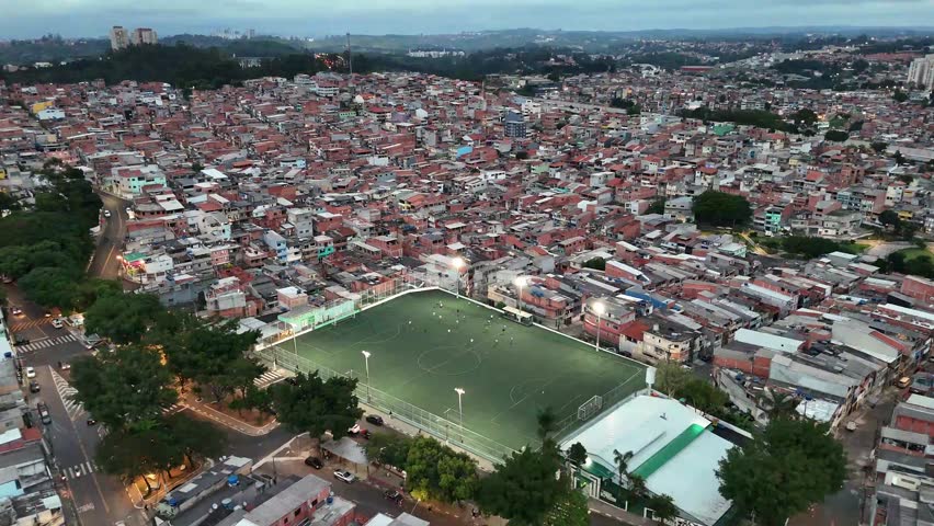 4k drone footage of a vibrant residential area in Osasco, Sao Paulo, Brazil, featuring a brightly lit soccer field in the middle of favela.
