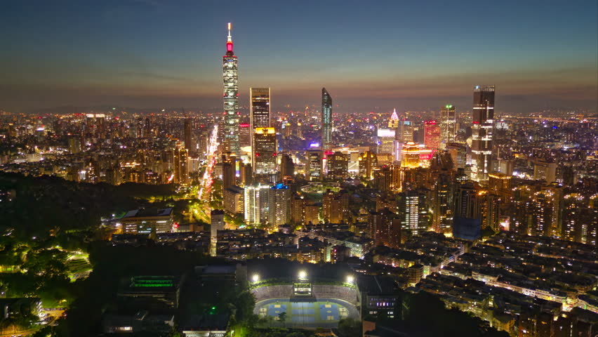 Aerial hyperlapse at sunset above Downtown Taipei, the vibrant capital of Taiwan, with 101 Tower standing out amid skyscrapers in XinYi Commercial District and city lights dazzling under twilight sky